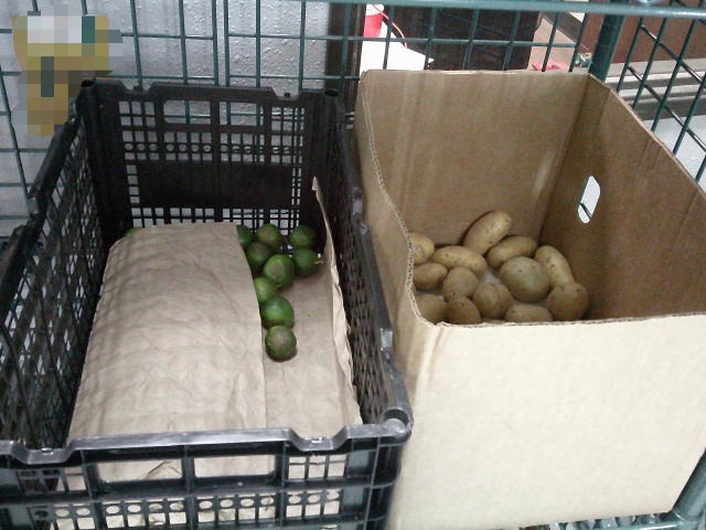 Limes on cardboard in a crate and a cardboard box filled with potatoes on a shelf.